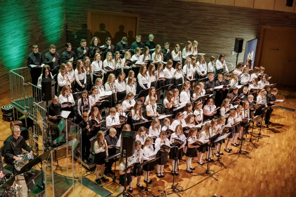 Zdjęcie z koncertu finałowego chórów Most the Music w 2023 roku. Liczna grupa śpiewających dzieci i młodzieży.