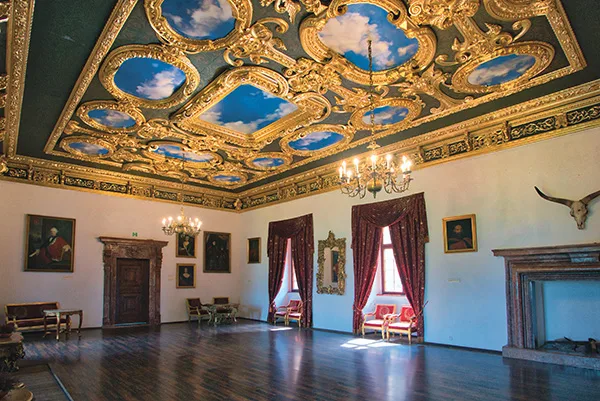 Wnętrze zamku: bogato zdobiona sala. Sufit ze złotymi elementami oraz malunkami imitującymi niebo i chmury.