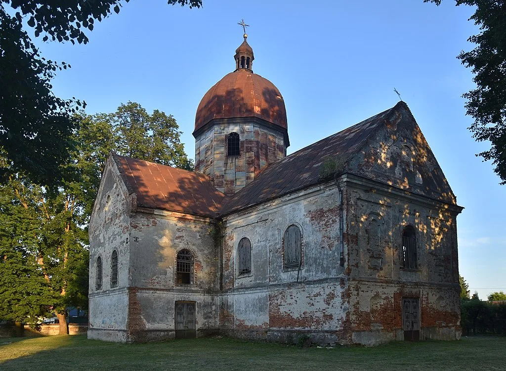 Murowana cerkiew z kopułą, w otoczeniu drzew.