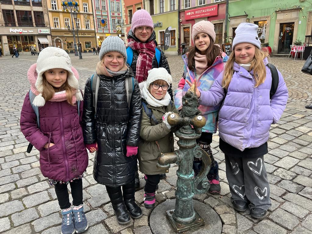 Zdjęcie: kilka dziewczynek z chóru Most the Music na rynku we Wrocławiu obok figurki krasnala.