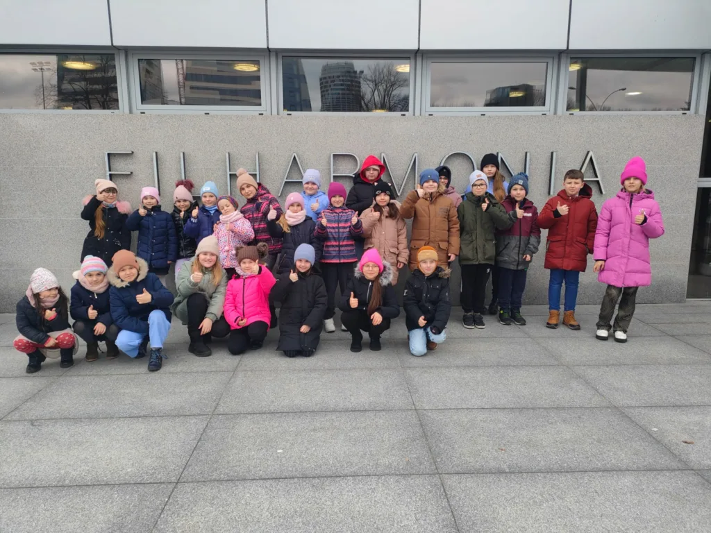 Zdjęcie grupowe dzieci i młodzieży przed Filharmonią Podkarpacką. Ubrane są w zimową odzież.