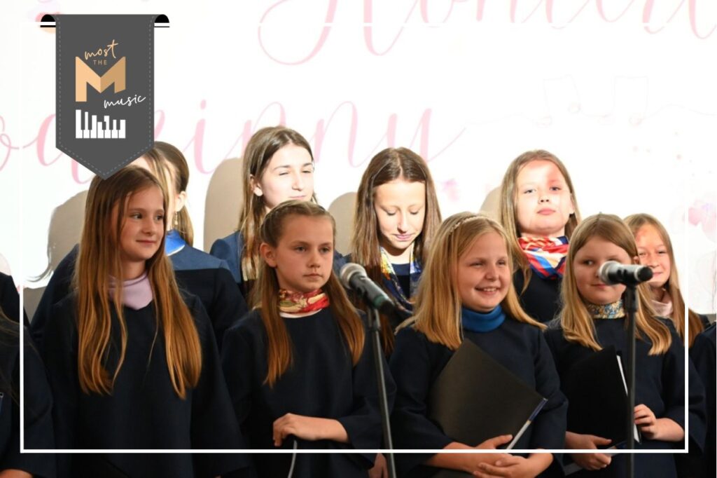 Zdjęcie chóru - grupa dzieci i młodzieży śpiewających na scenie.