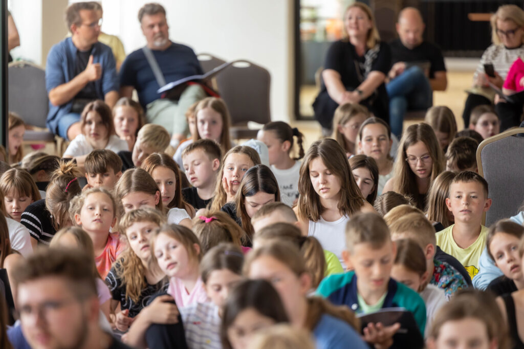 próba śpiewu - dzieci i młodzież. w tle chórmistrzowie.