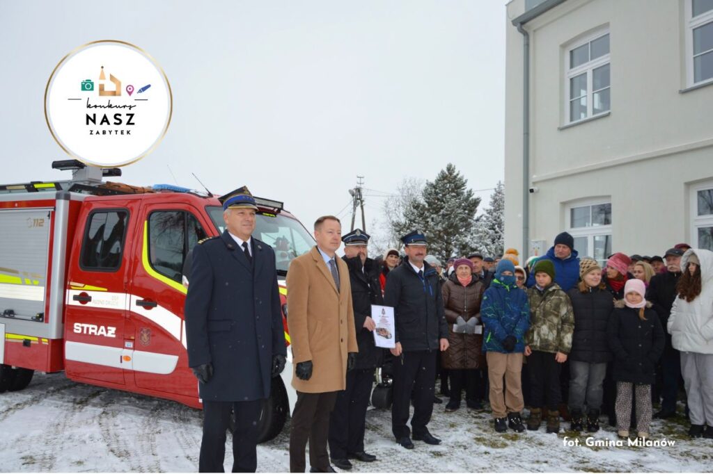 Uroczystość otwarcia domu strażaka w Rudnie. Grupa ludzi (w tym uroczyście ubranych strażaków) przed zabytkiem i wozem strażackim.